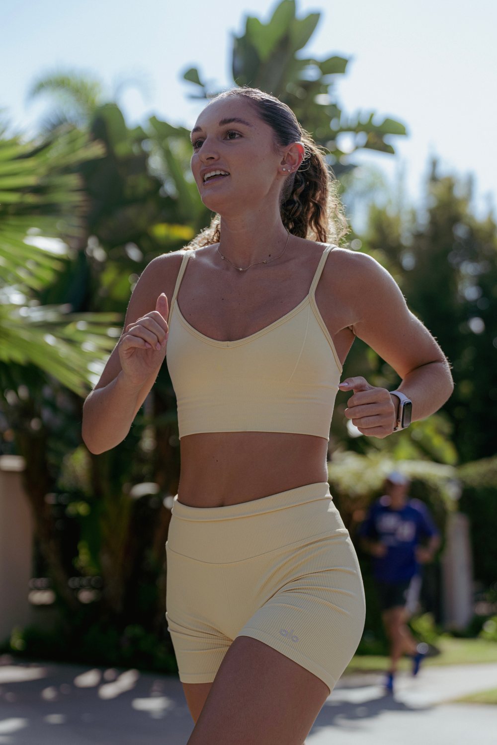 Julia mid-run on a sunlit path lined with palm trees