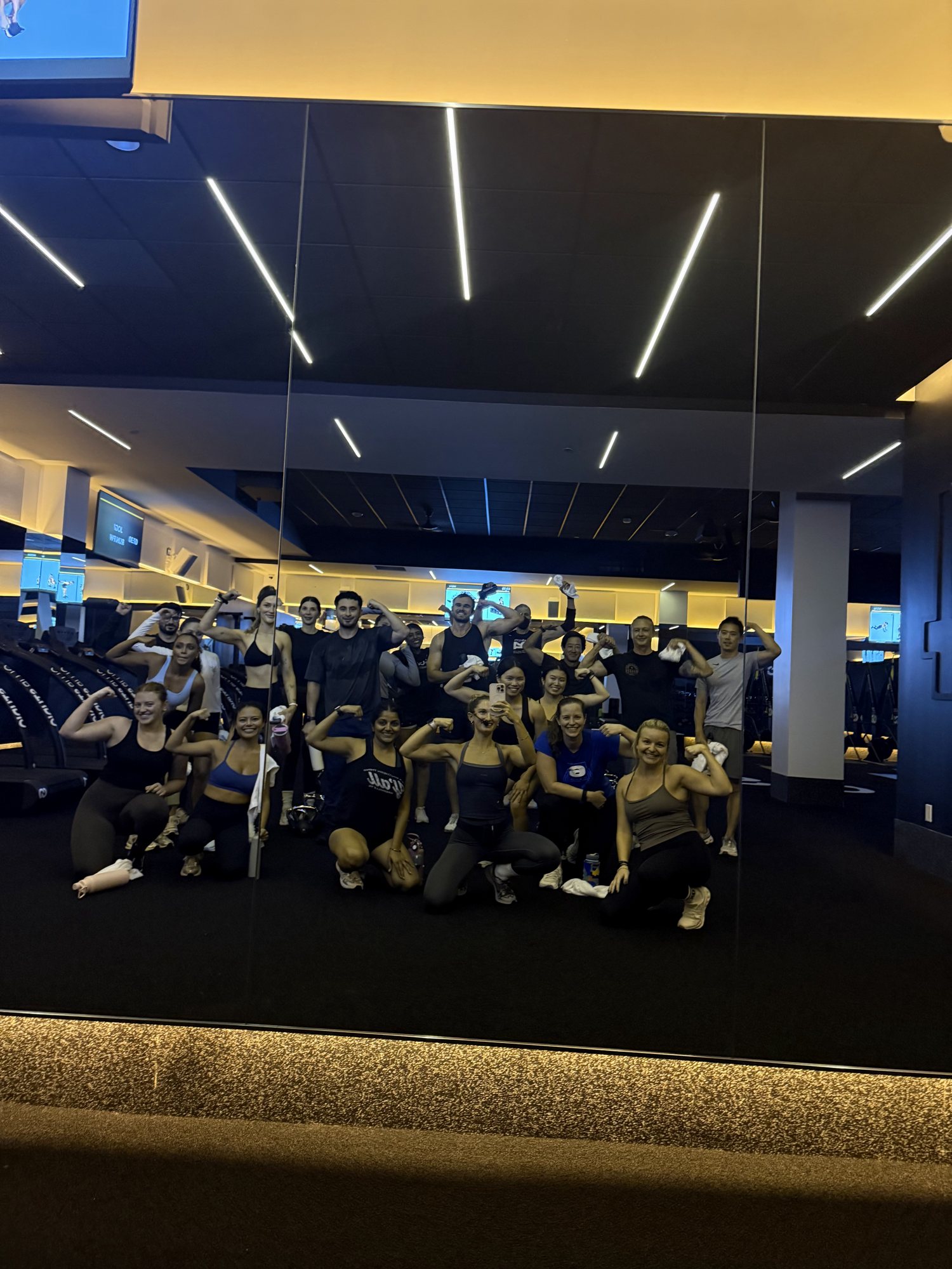 A group flexing and smiling together in a gym with a mirrored wall